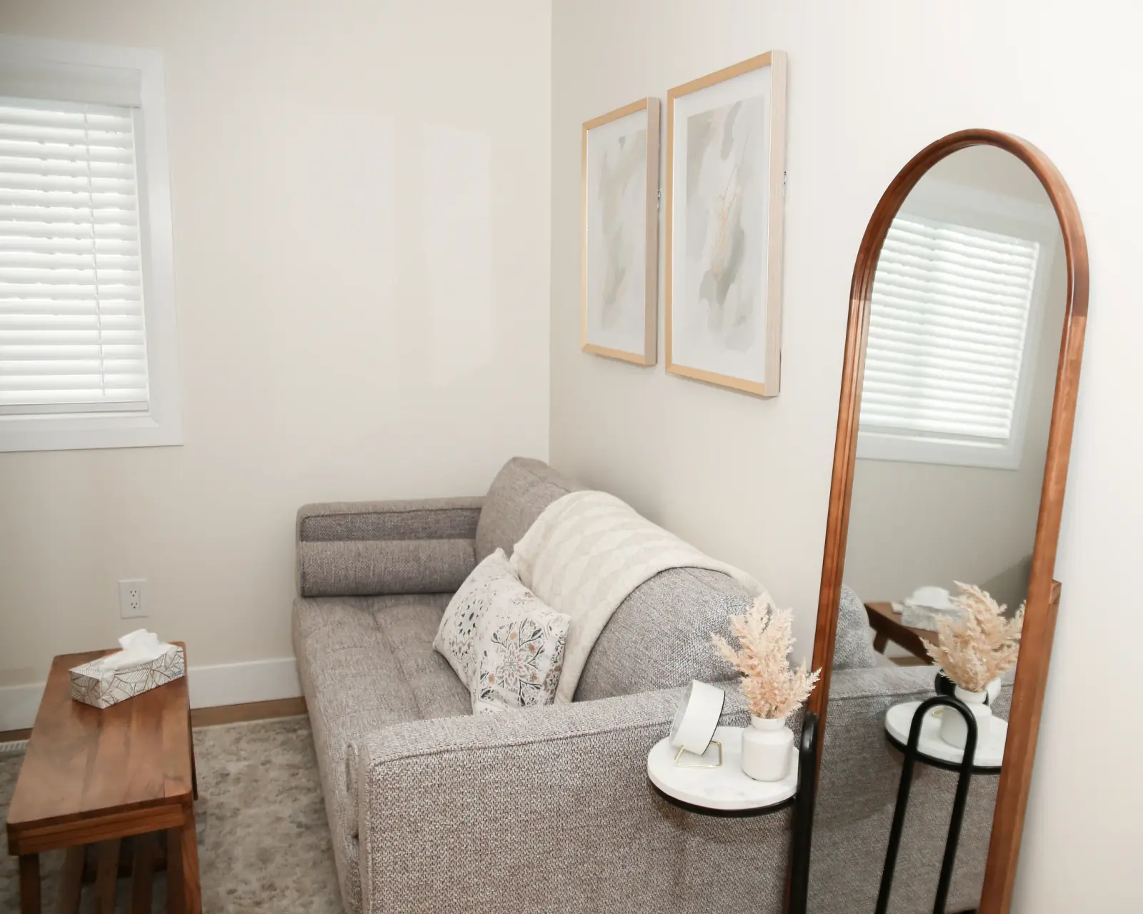 A neutral KDW Counselling therapy room with a sofa, chair, and warm framed mirror.